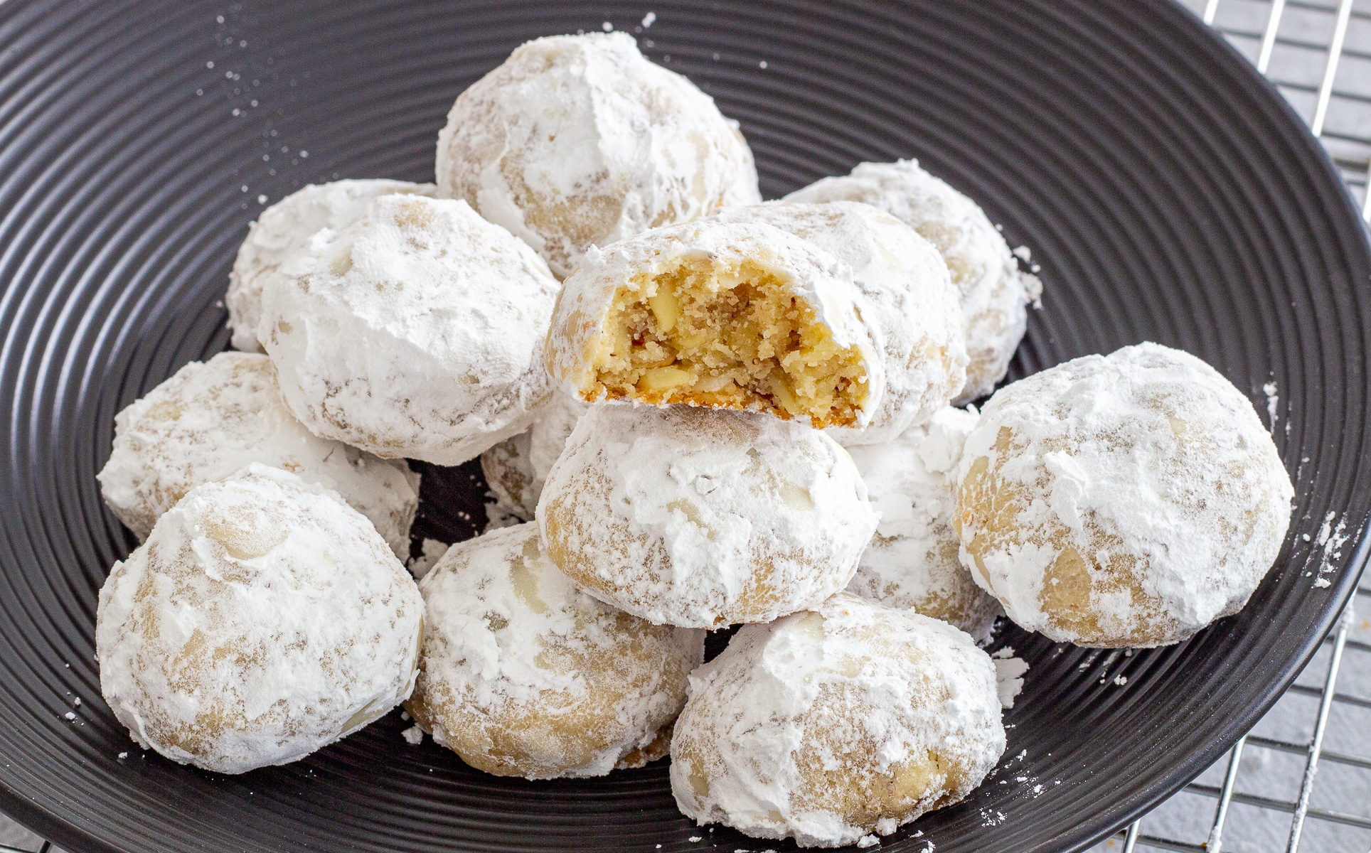 a black plate filled with sugar covered cookies, one with a bite taken out of it
