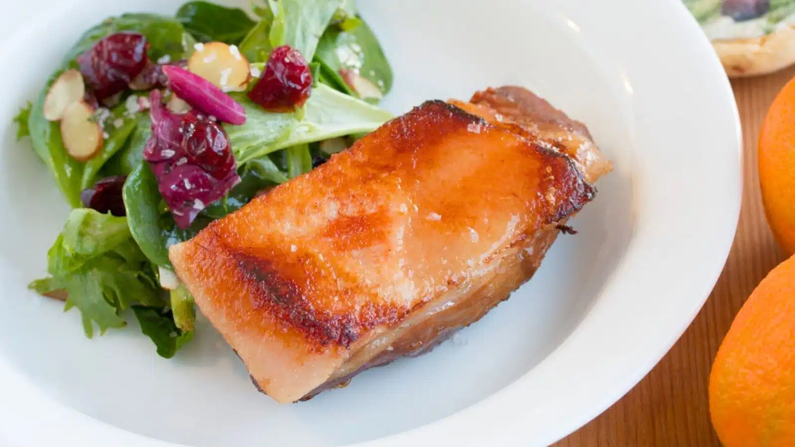 pork belly with a sauce on a white plate with a salad