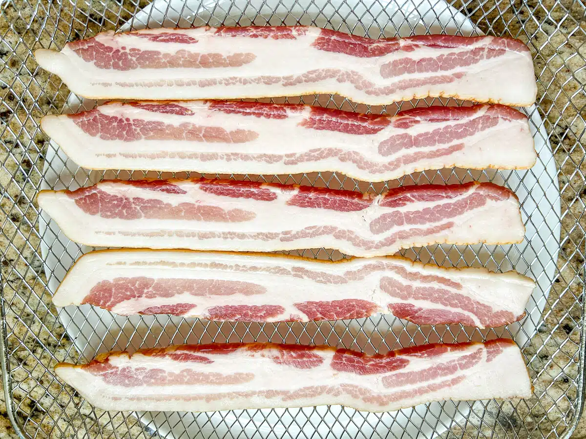 A wire rack with five pieces of raw bacon on it.
