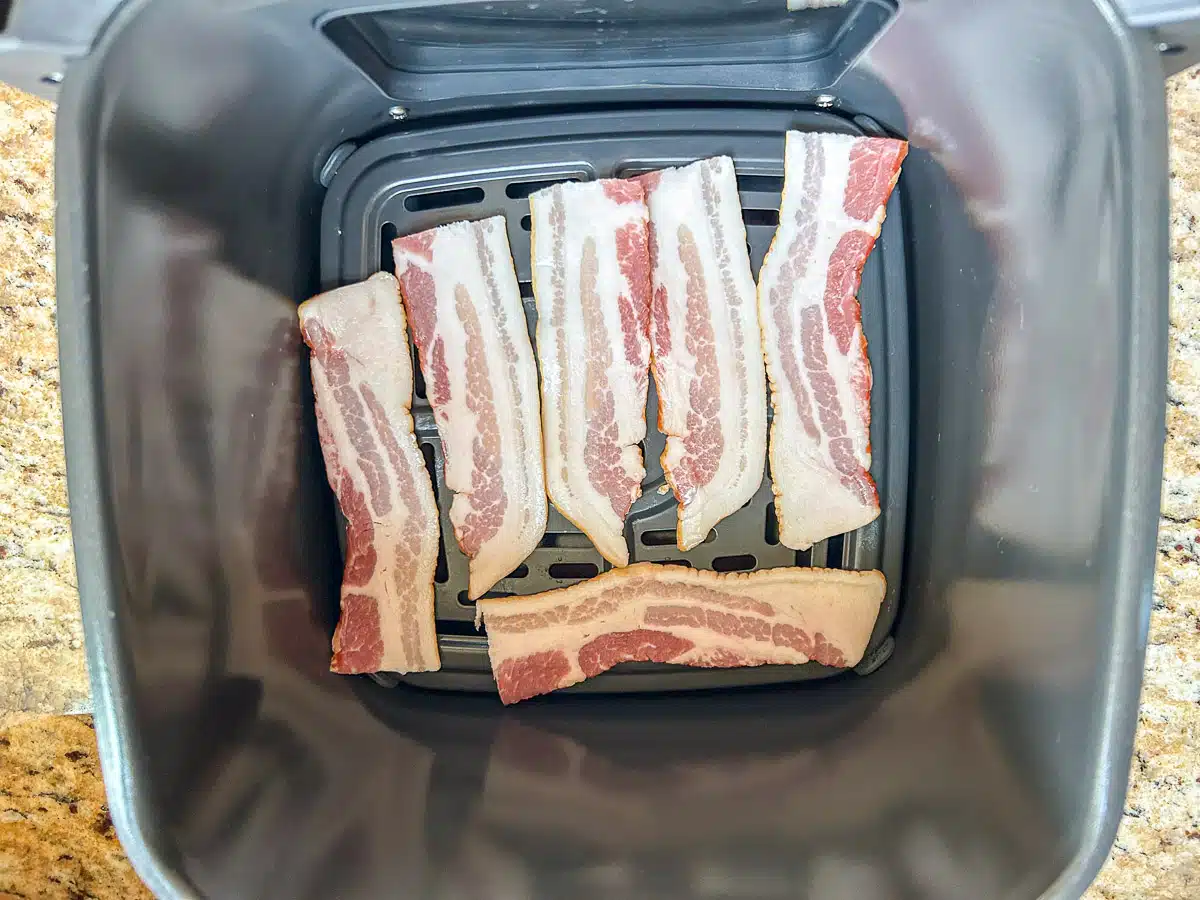 A basket type of air fryer with three pieces of bacon cut in half