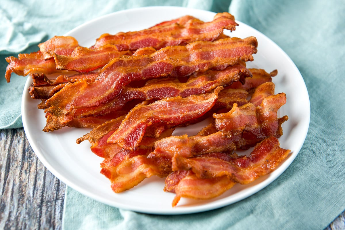 a green napkin with a white plate and cooked bacon on it