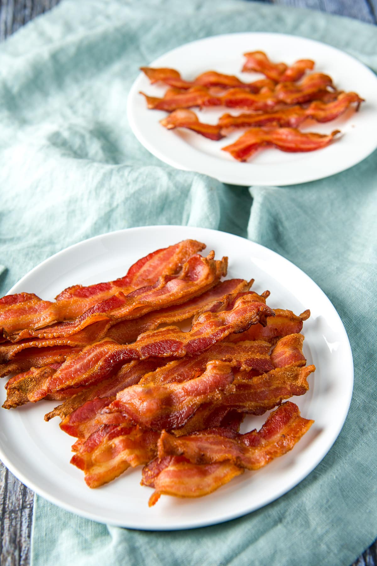 Two plates with cooked bacon on it on a green napkin