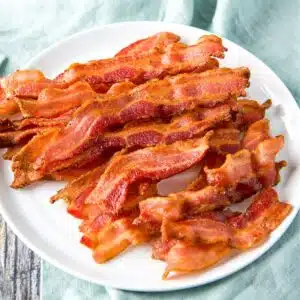 a square photo of a white plate of cooked bacon