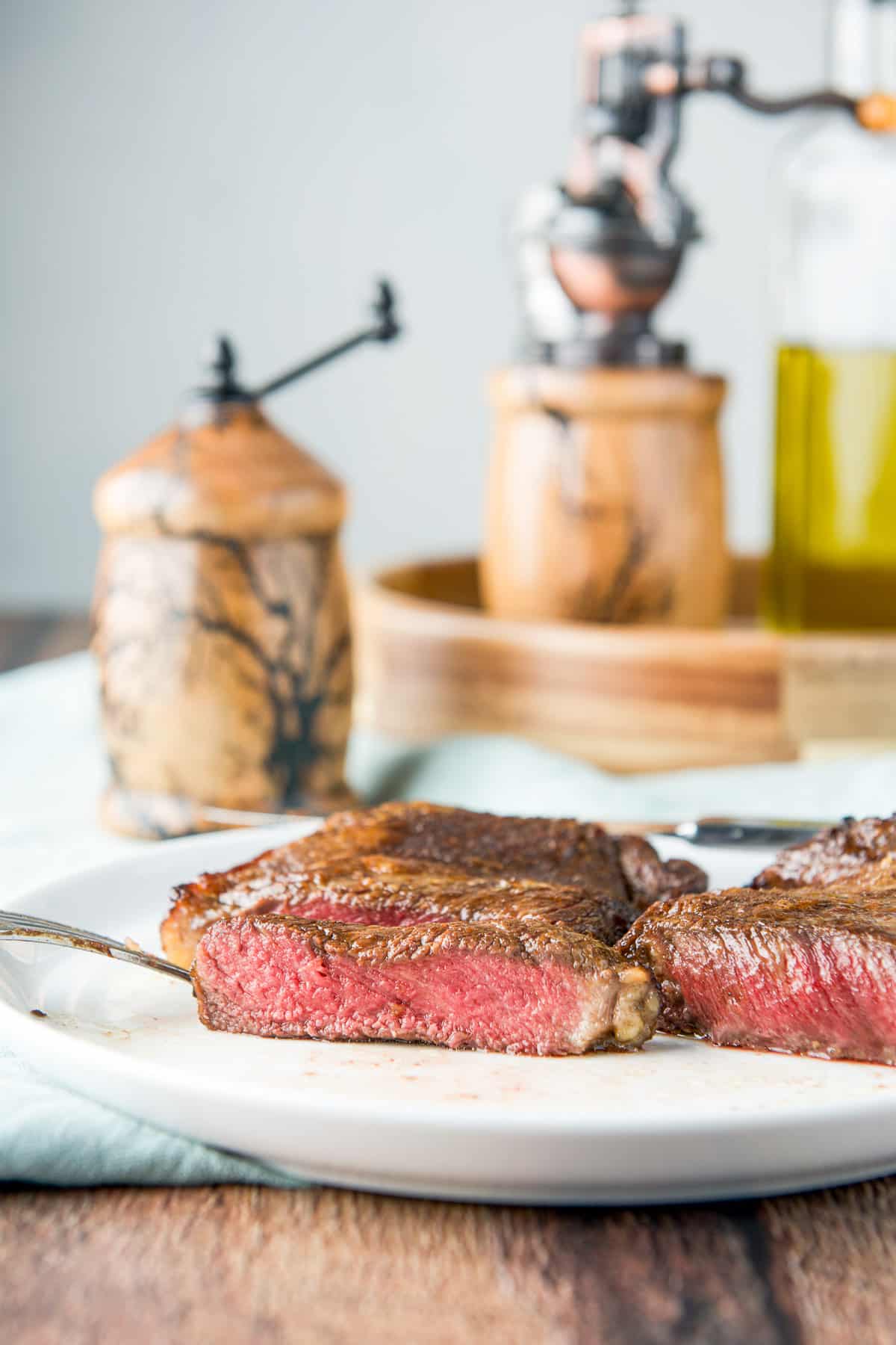 Vertical view of the medium rare steak on a white plate with condiments in the back