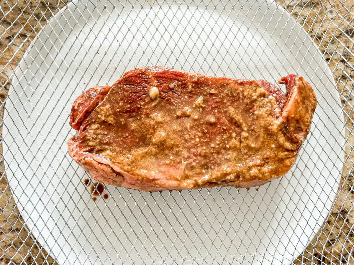A raw steak on the air fryer basket tray over a white plate