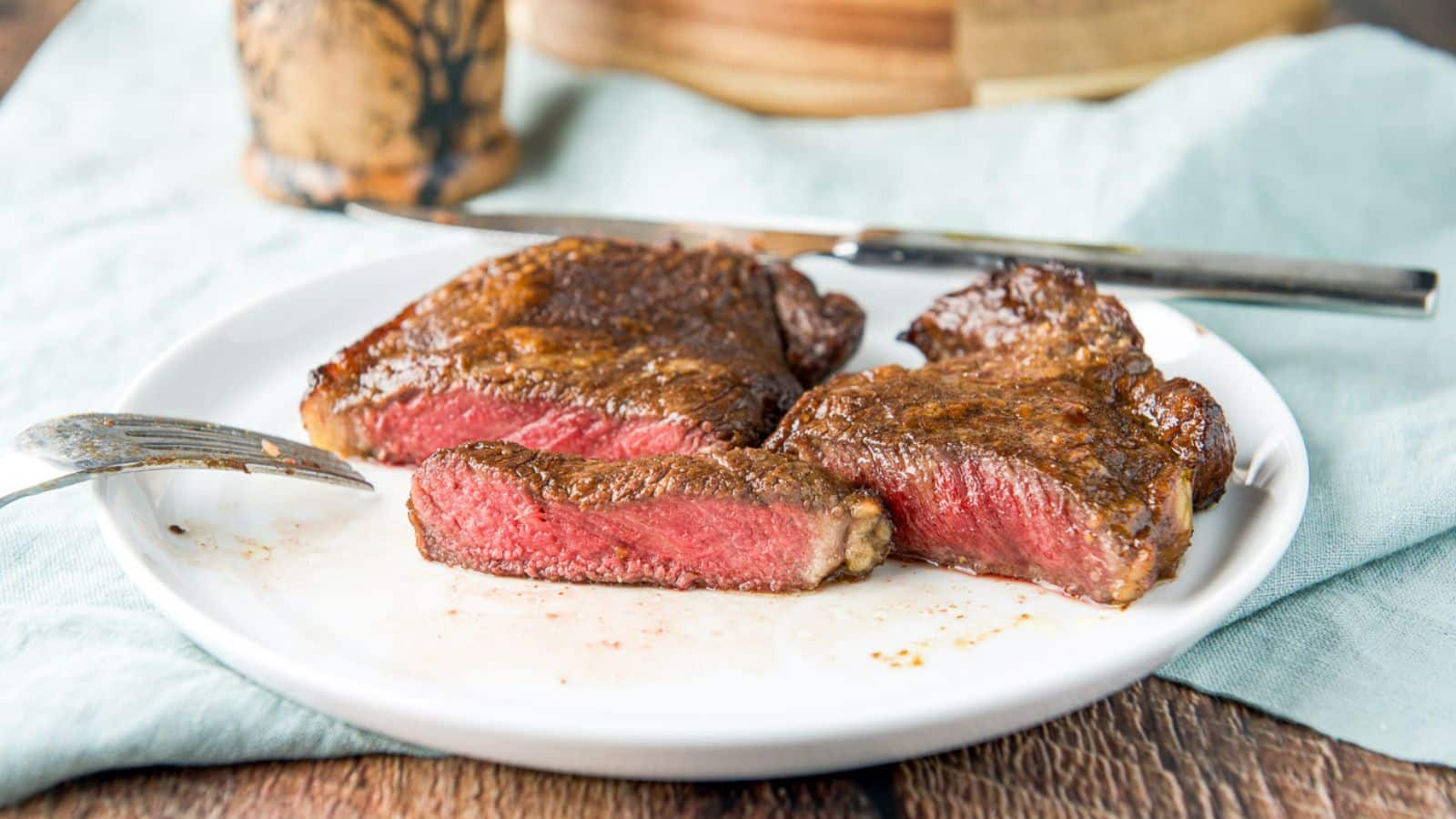 A white plate with a medium rare steak cut in half and a piece cut out of it
