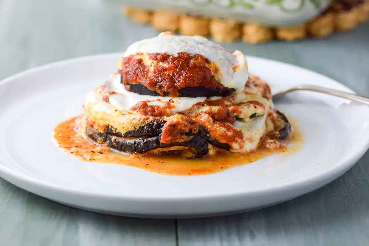 a white plate with three pieces of eggplant, sauce and cheese stacked on each other