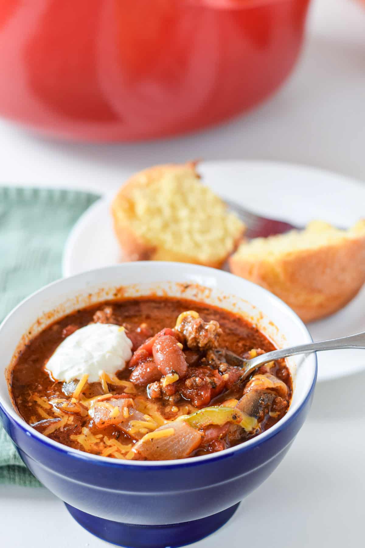 A blue bowl with chili and sour cream in it with a corn muffin and red pan