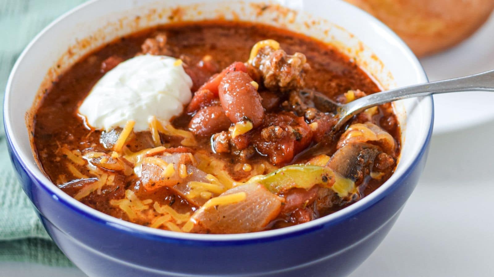 a blue bowl with chili in it, along with cheese and a dollop of sour cream