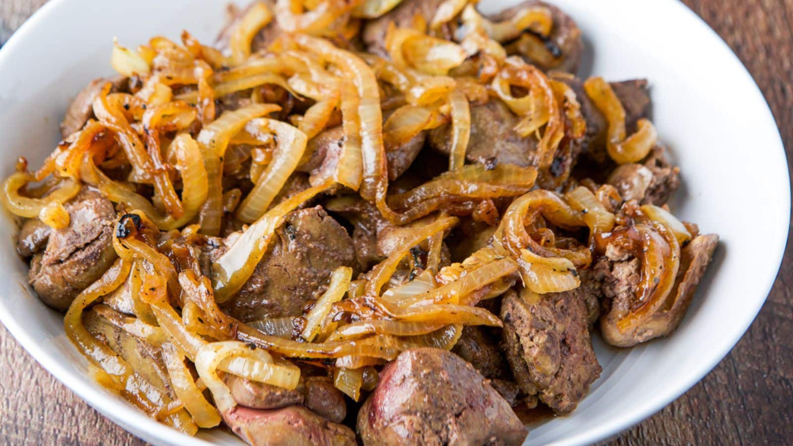 a white deep plate with chicken livers and onions in it