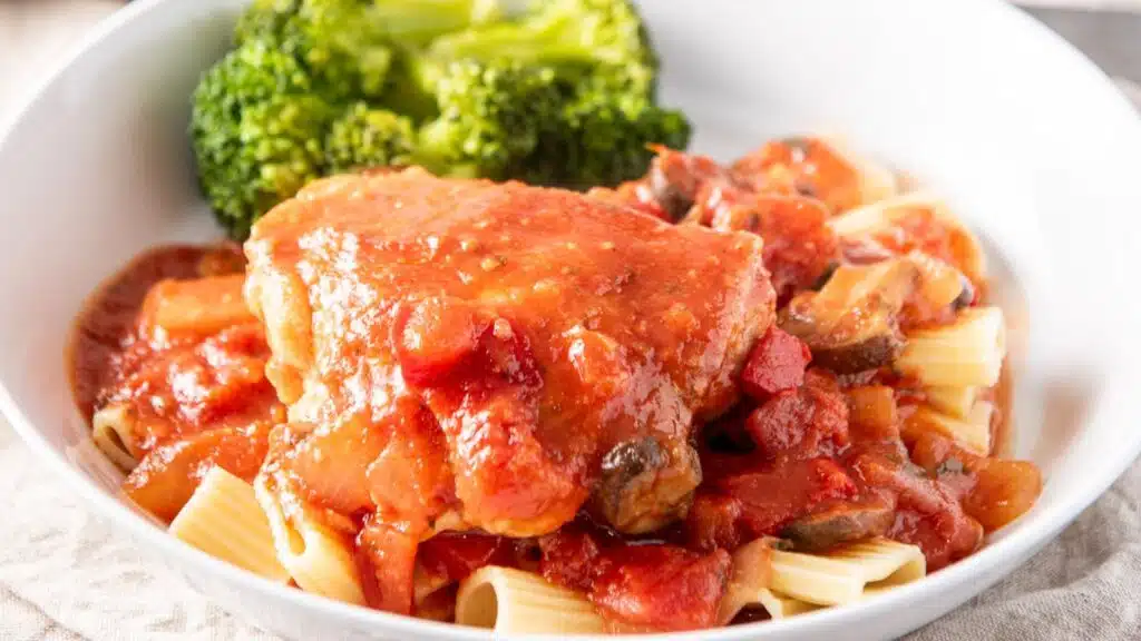 A white plate with pasta with chicken and sauce on it along with broccoli