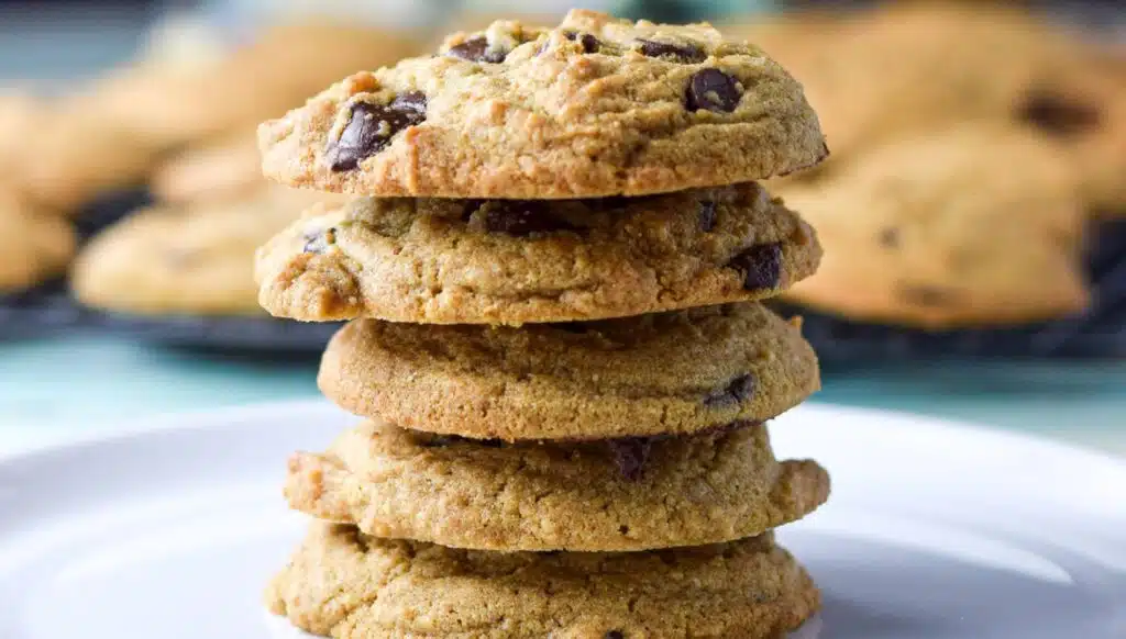 A pile of chocolate chip cookies one on top of the other with wire racks filled with the cookies