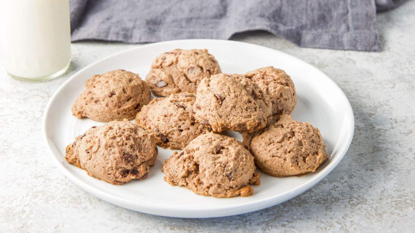 A small plate with chocolate cookies piled on it along with a glass of milk