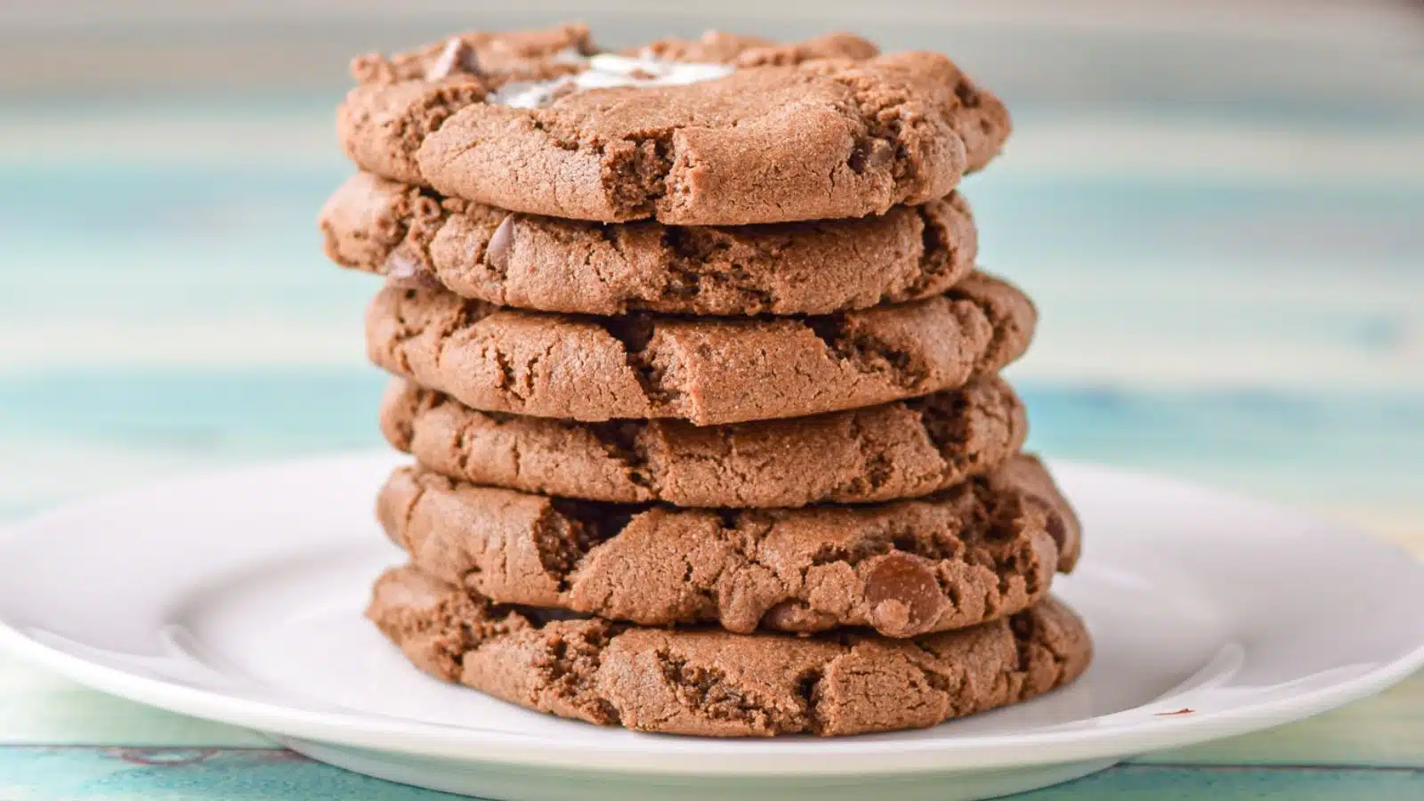 a white plate on a blue table with six chocolate cookies in a stack