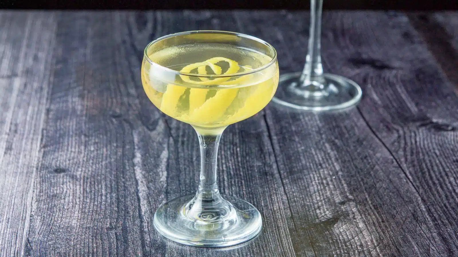 A coupe glass filled with the clear cocktail with lemon twists