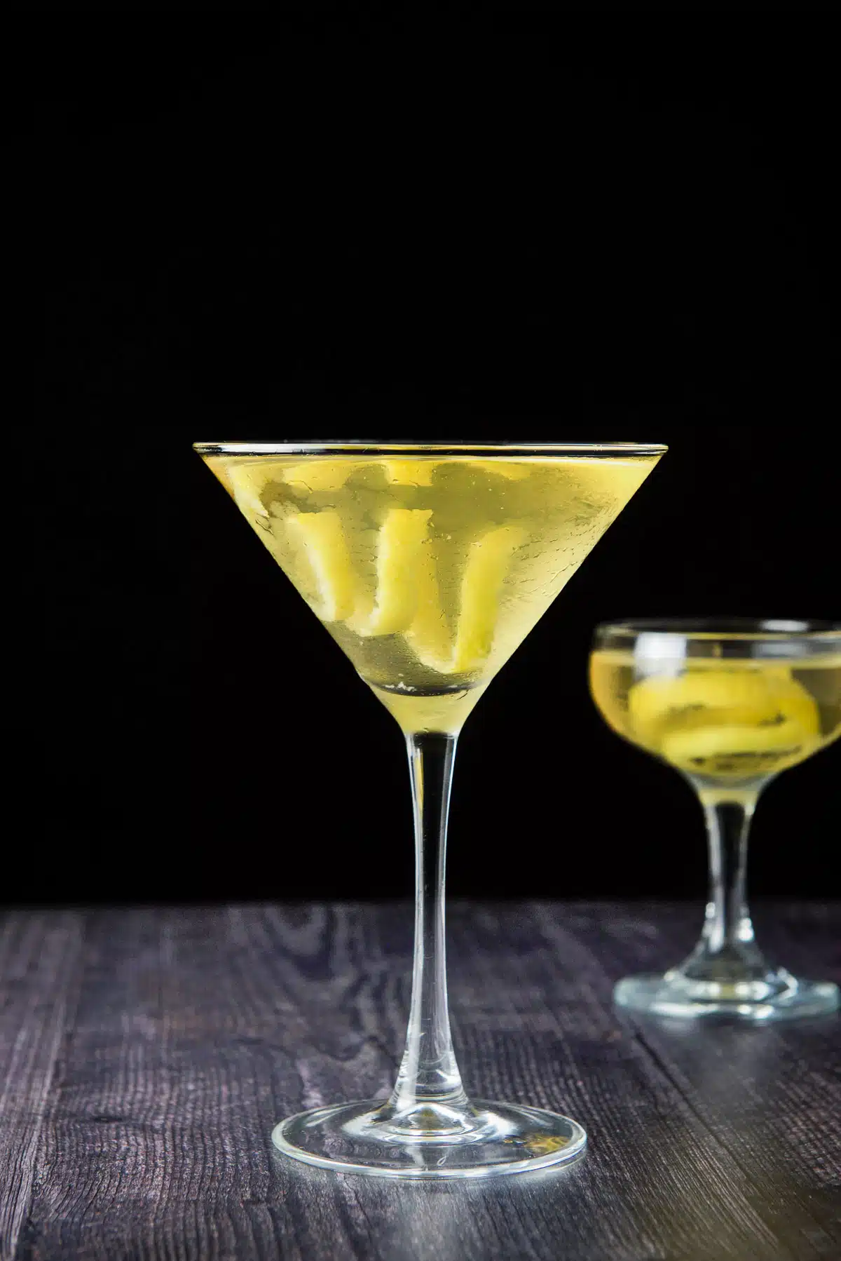 vertical view of the two martini glasses filled with the clear cocktail with lemon twists