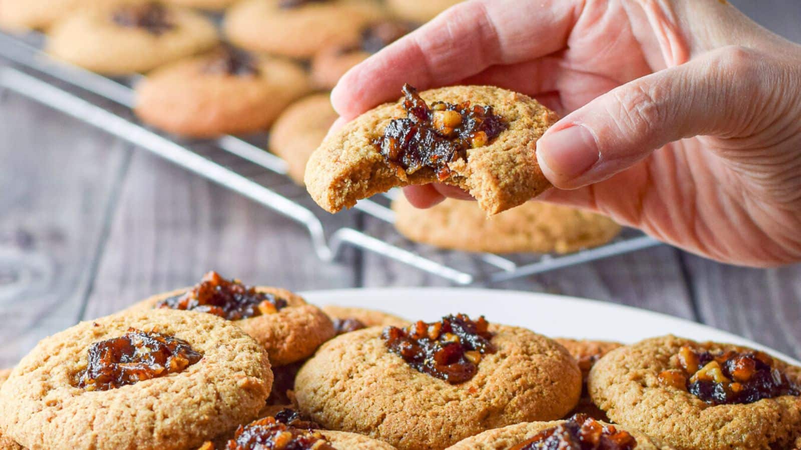 A hand holding a date cookie with a bite taken out of it, held over a plate of cookies