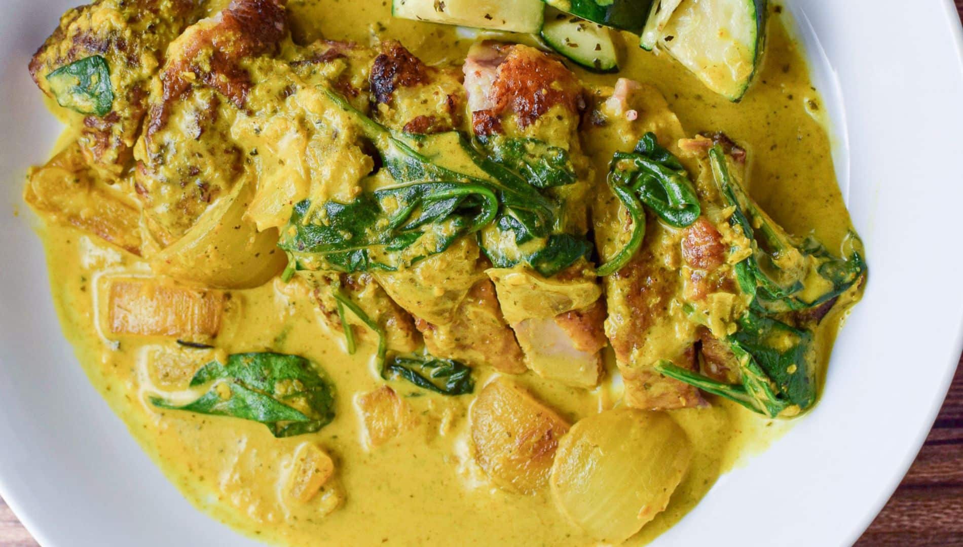 overhead view of a white plate with duck breast with curry sauce poured over it along with spinach