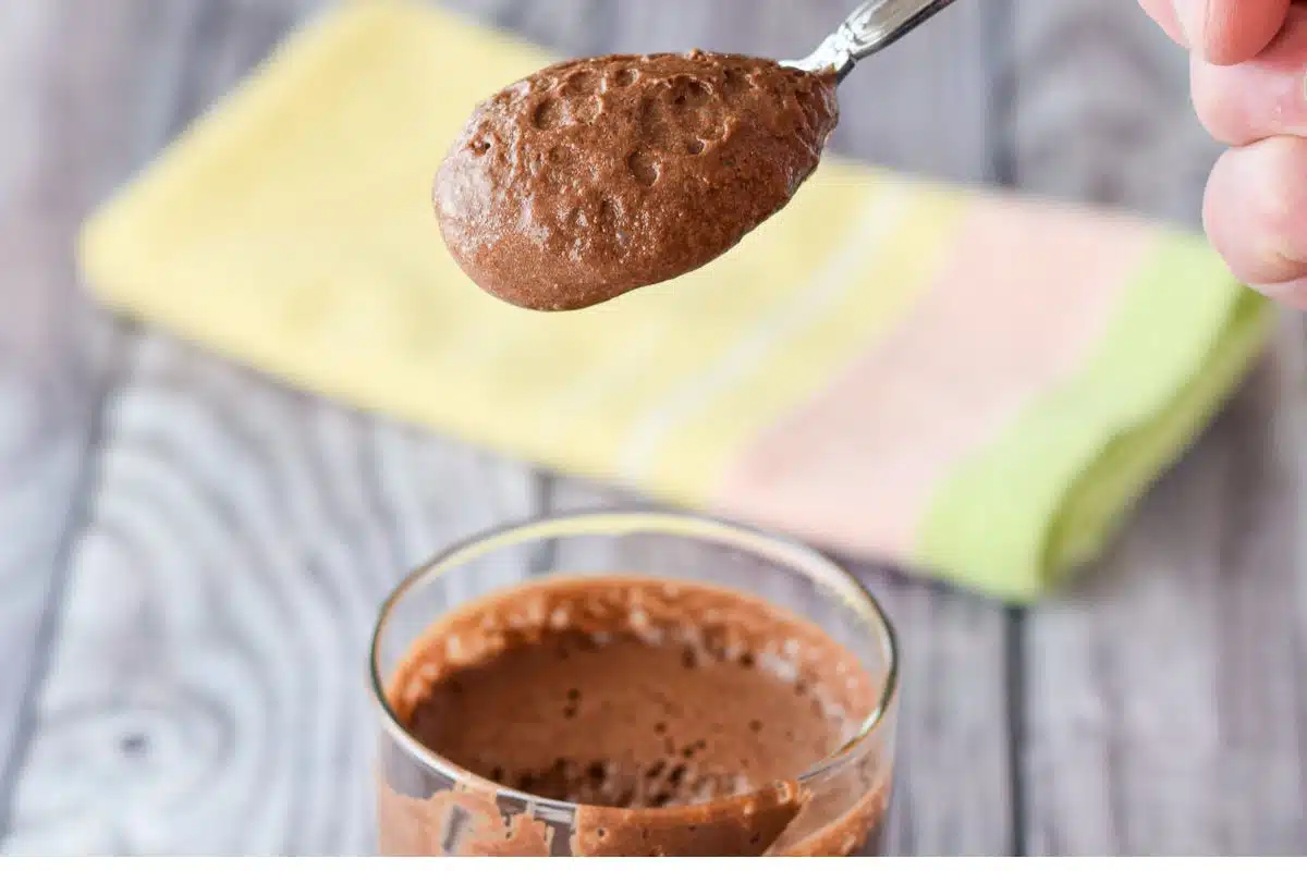 A hand holding a spoonful of mousse over the glass of it