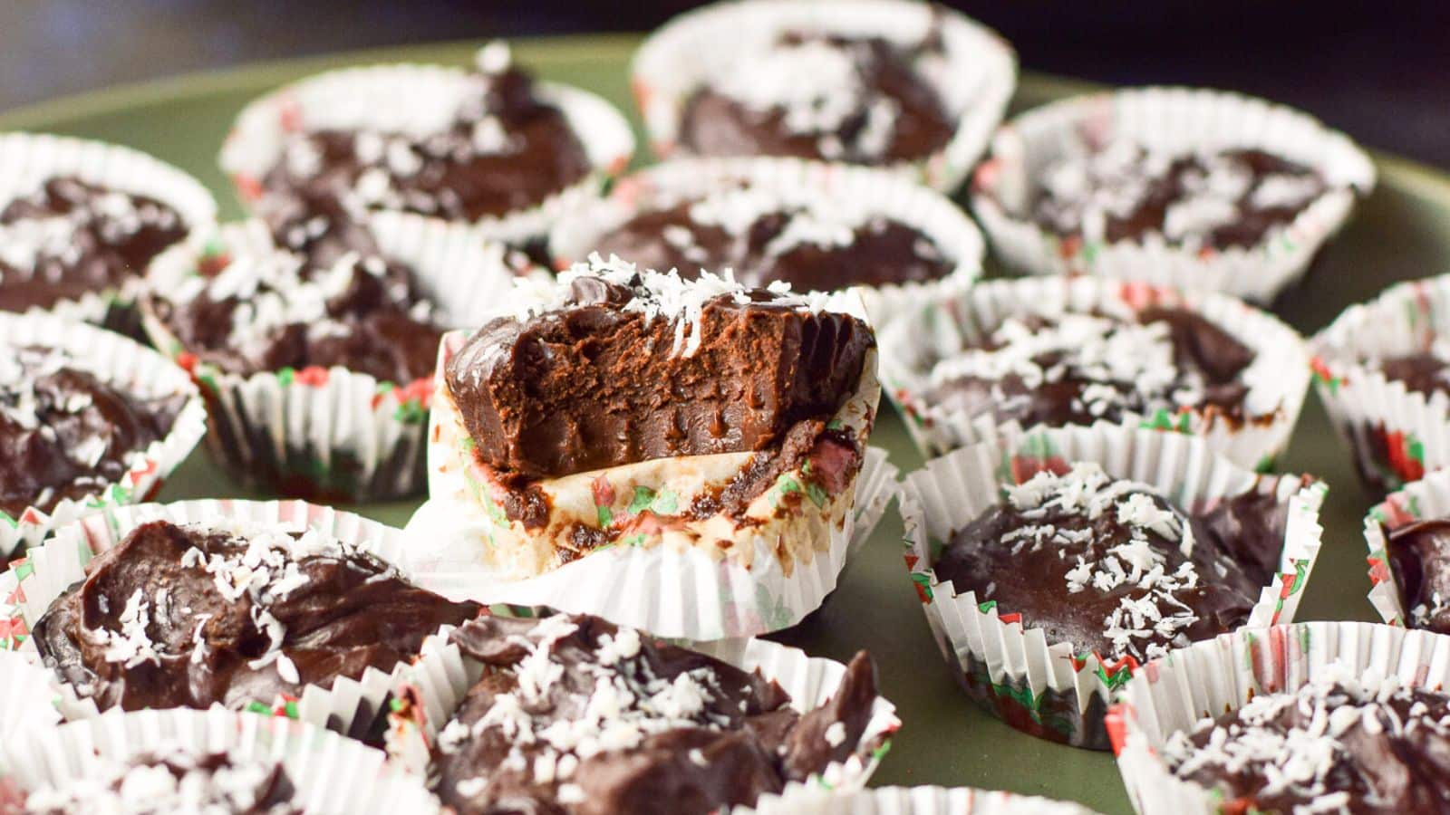 coconut sprinkled chocolate truffles in paper cups on a plate with one with a bite taken out of it