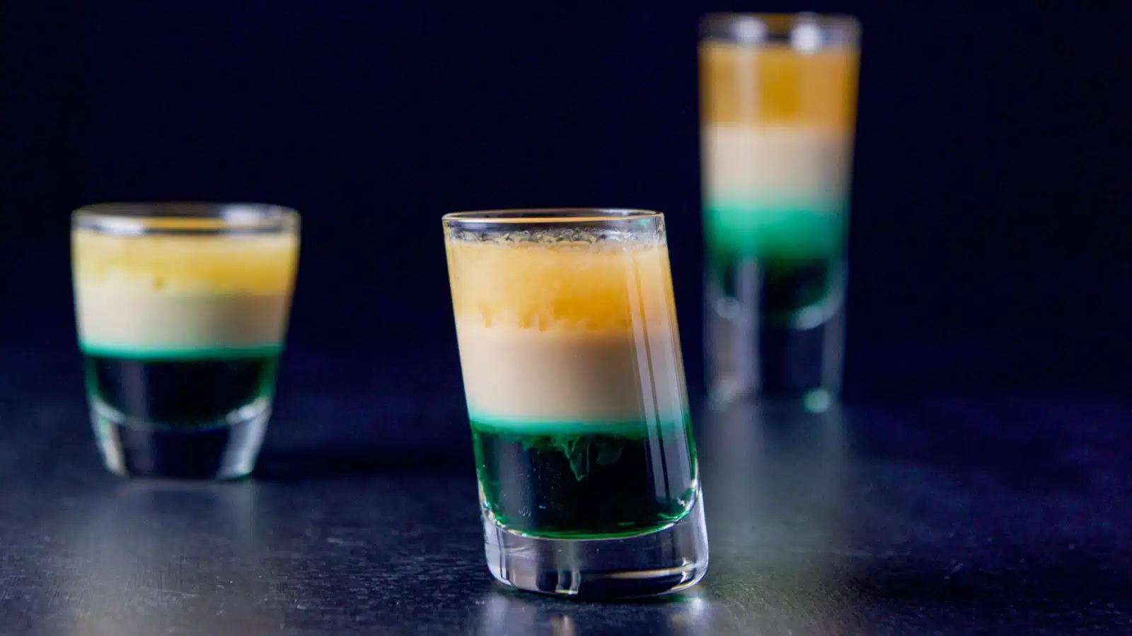 Three shot glasses layered with the green, tan and brown liqueur