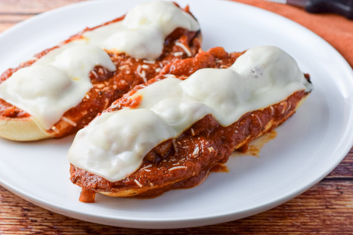 A white plate with two halves of a red sauce ladled on bread with meatballs and melted cheese