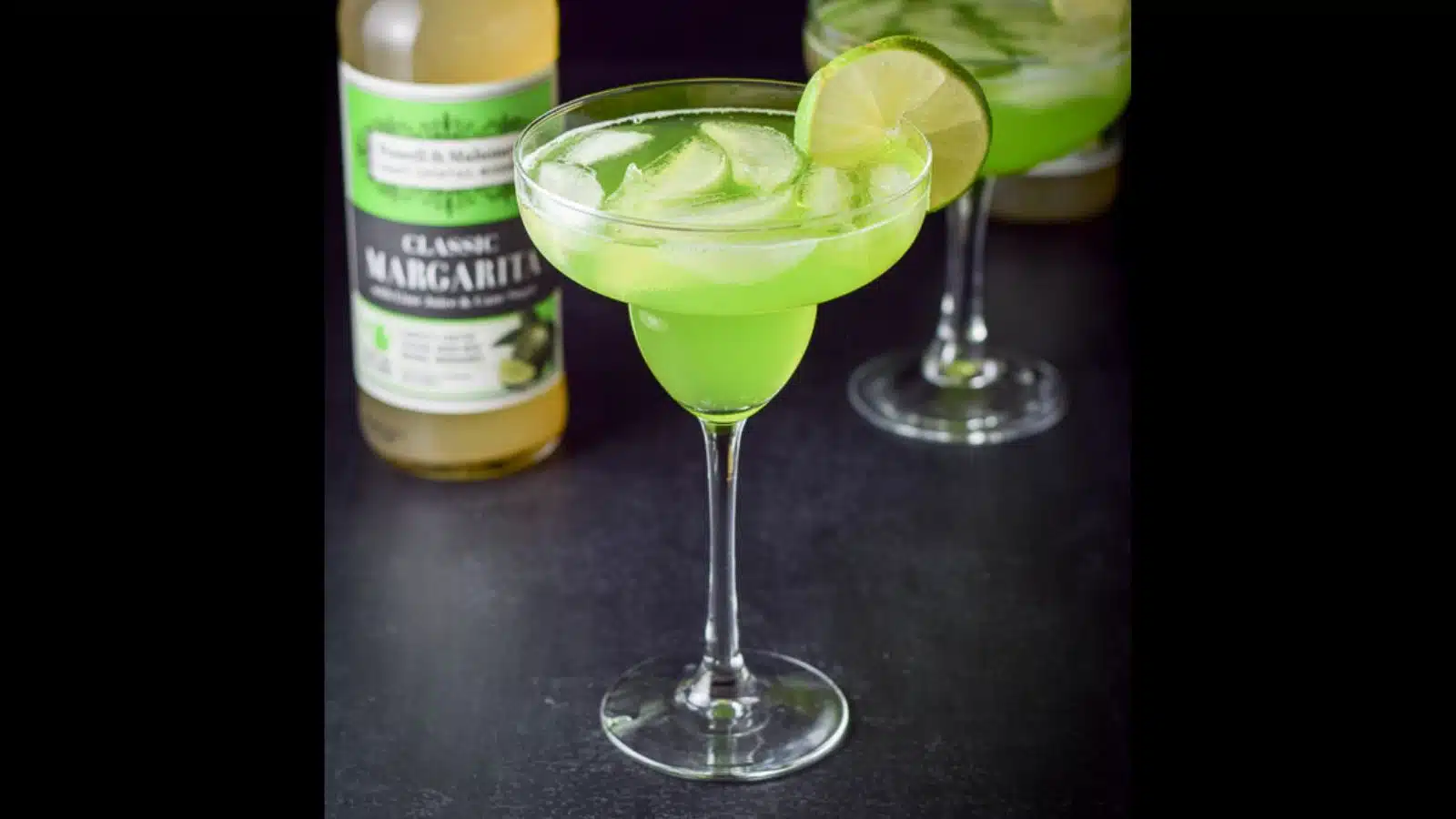 A classic margarita glass filled with a melon margarita with lime as garnish