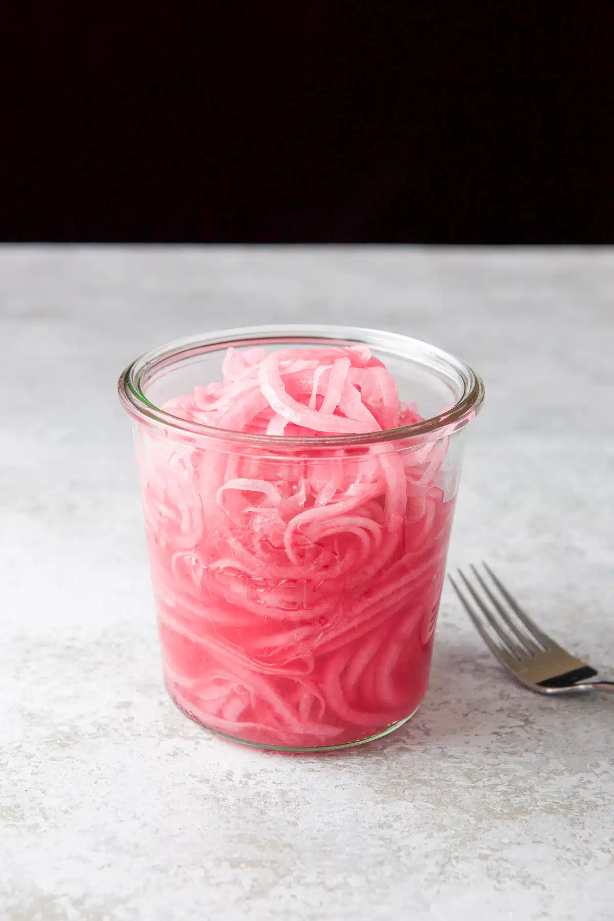 A fork on the table with an open jar of pickled red onions