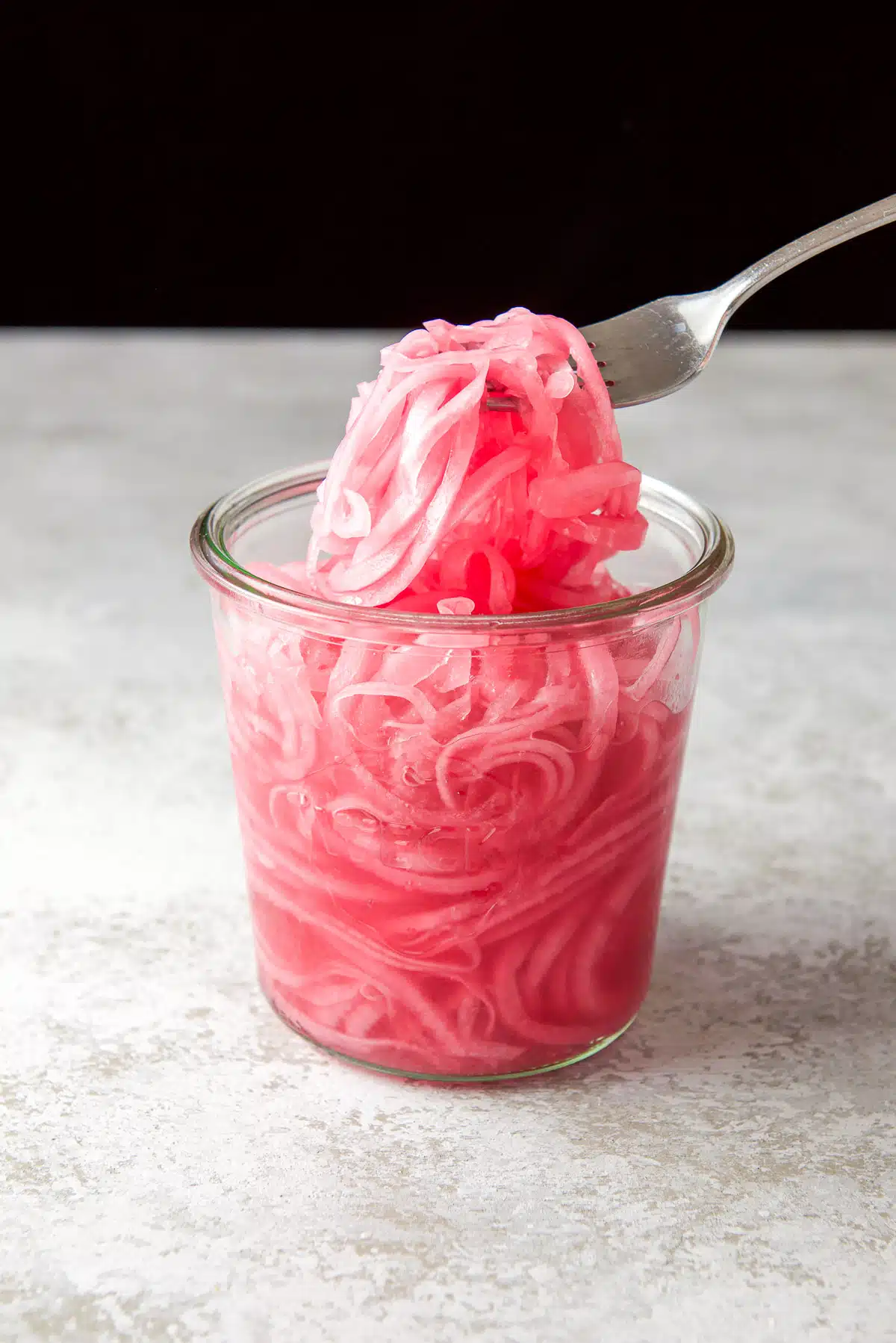 A fork holding the onions out of the jar of pickled red onions