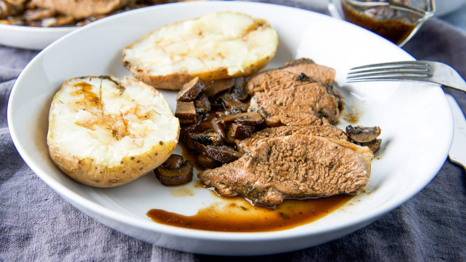 A white deep plate with a potato, mushrooms and pork tenderloin with a sauce