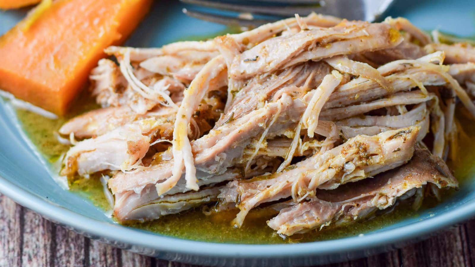 A deep blue plate with pulled pork on it with vegetables