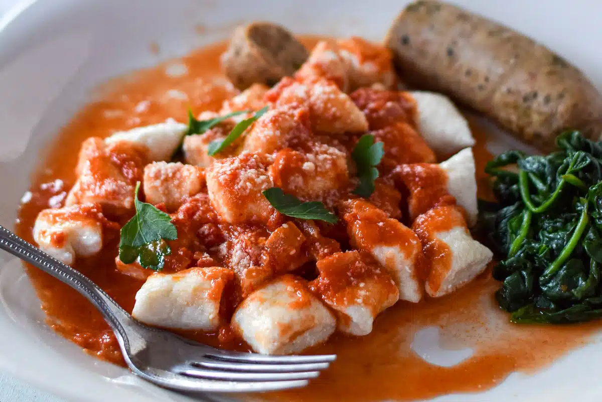 gnocchi and sauce on a plate with a sausage and spinach