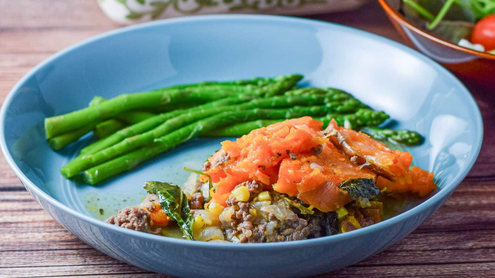 A blue deep dish filled with ground beef, corn, and other vegetables and cooked yam on top