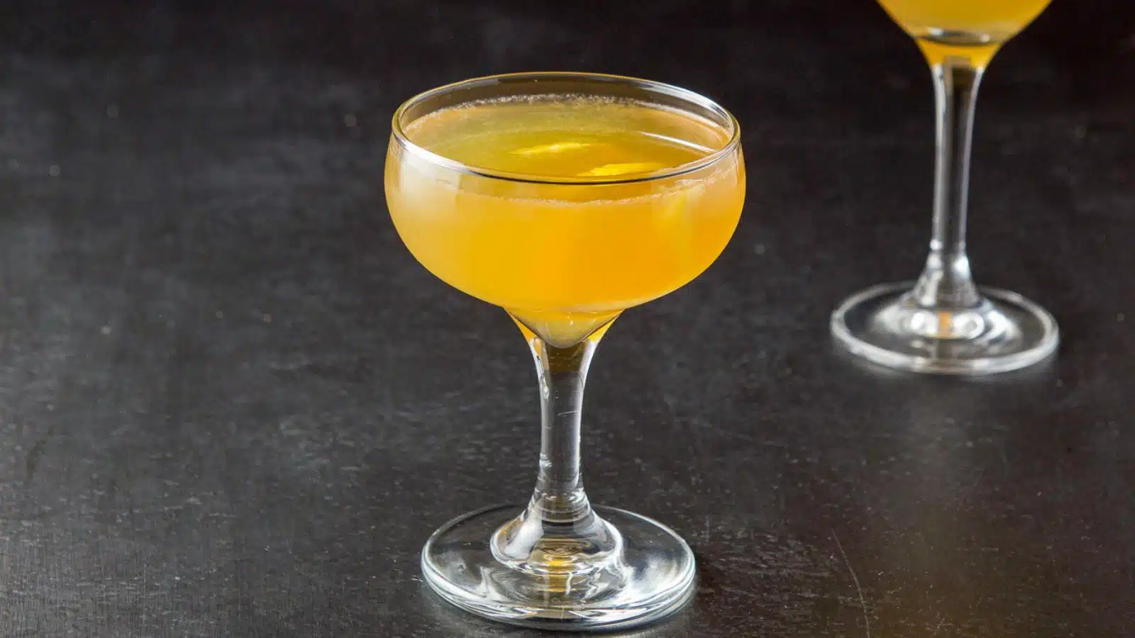 a coupe glass filled with an orange cocktail with a lemon twist in as garnish