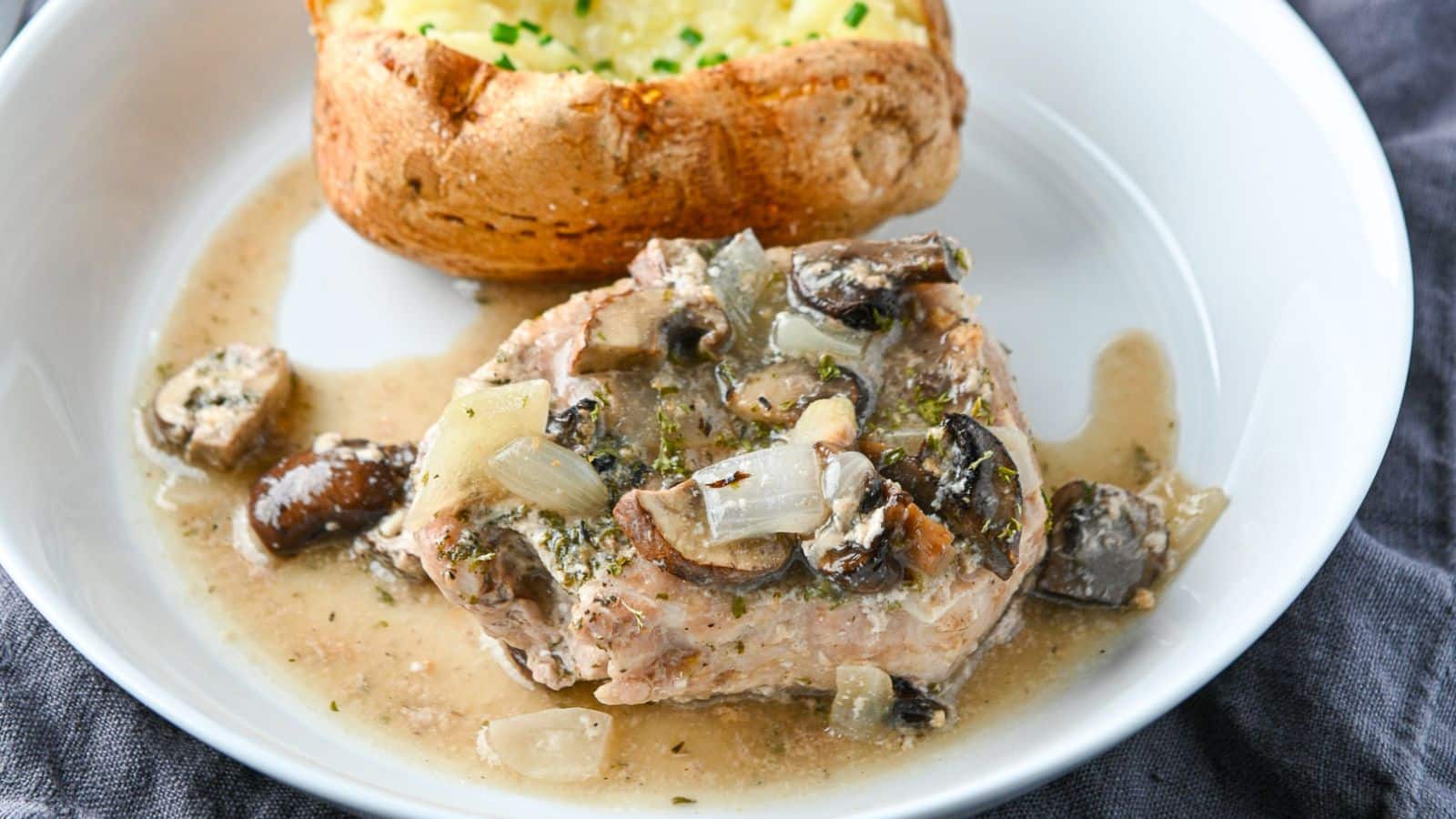 A white deep plate with the mushroom and onion sauce on a pork chop with a potato