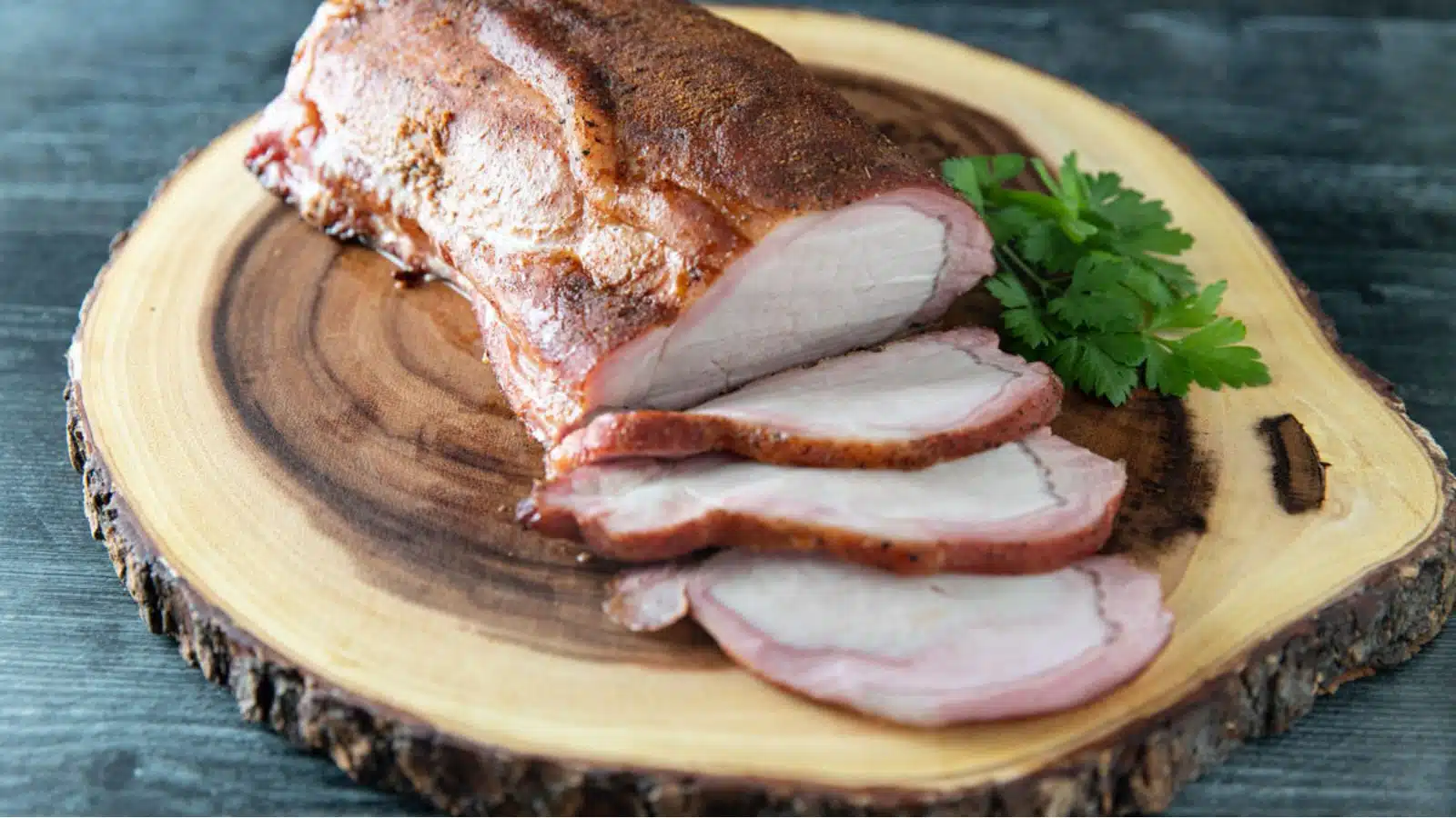 A wood tray with a pork loin on it with some parsley
