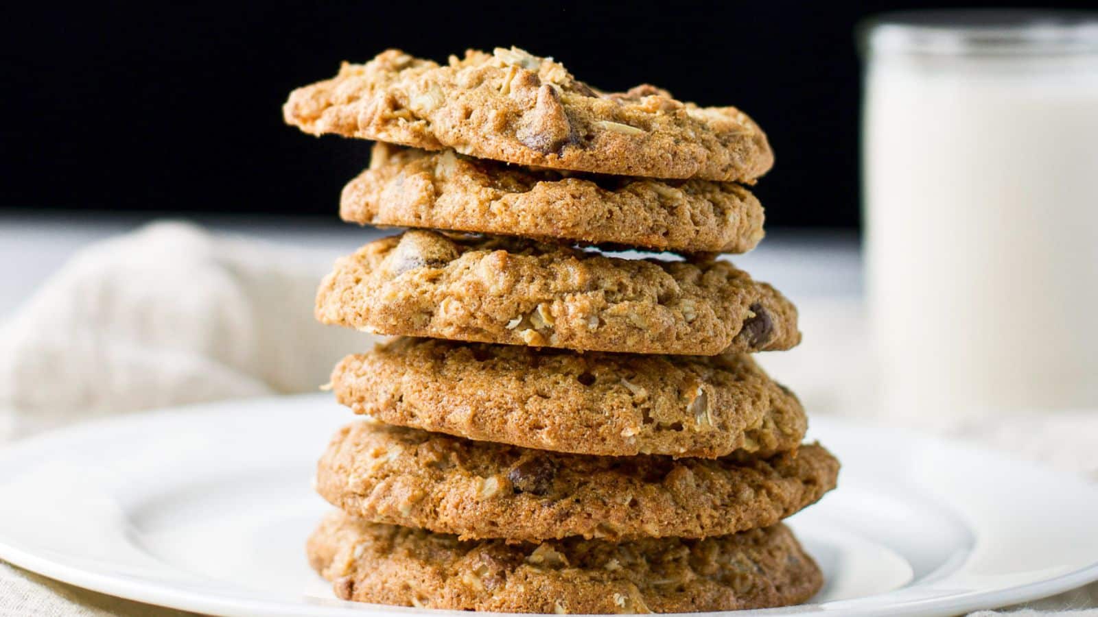 A plate with a stack of snickers cookies on it along with a glass of milk in the back