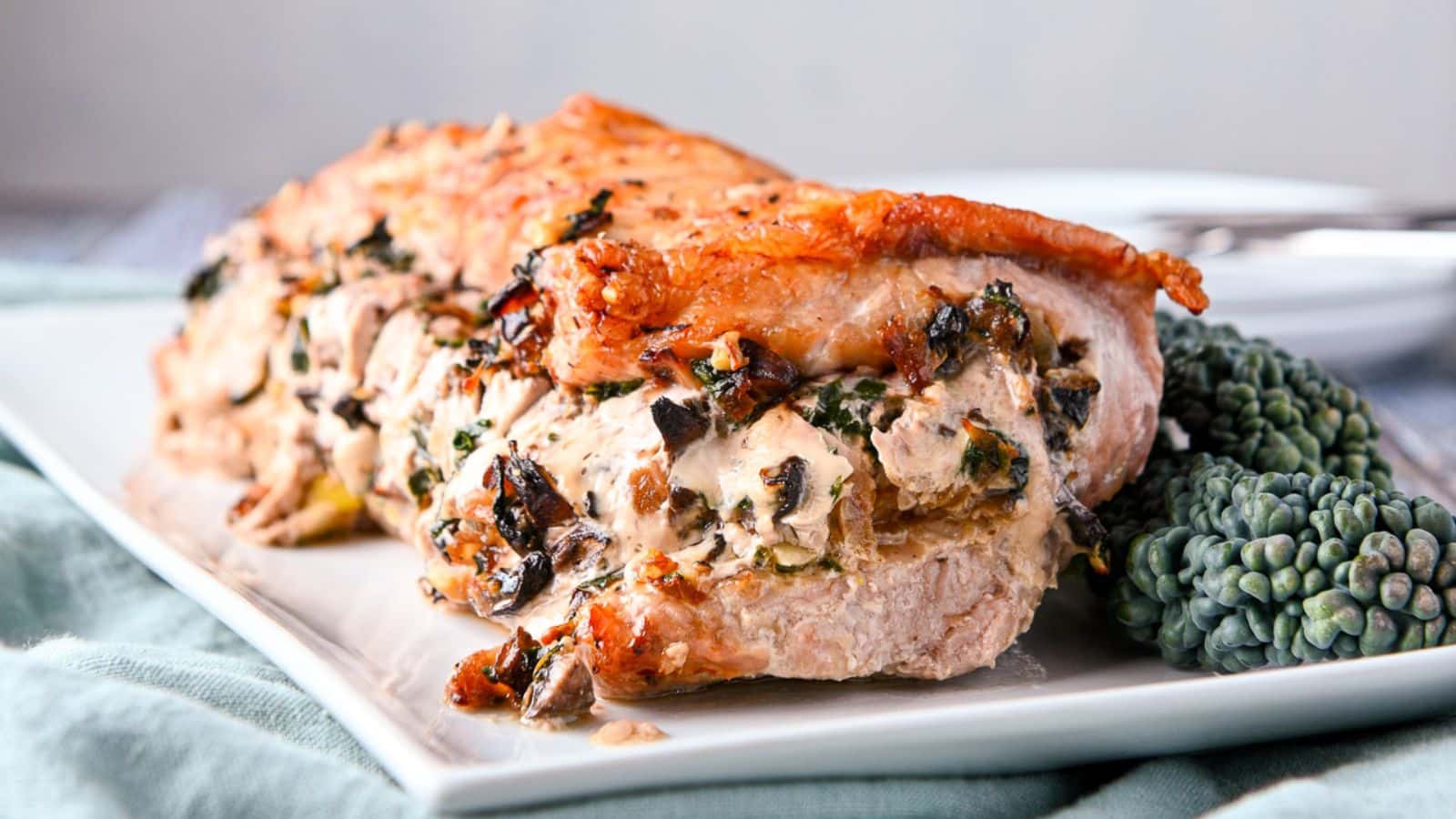 A rectangle platter with a stuffed pork on it with kale on the side