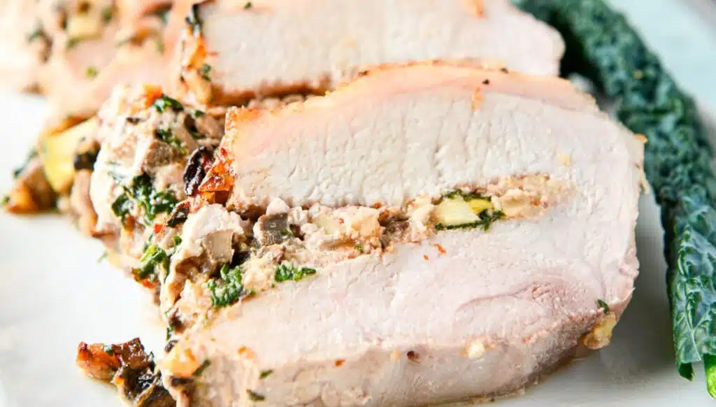 Close up of stuffed pork on a white platter with kale as garnish