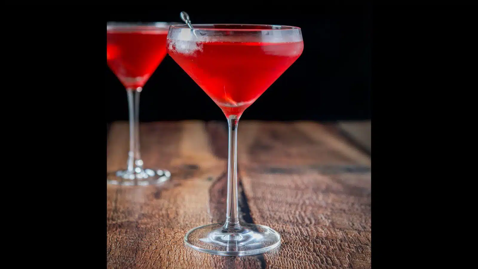 A curved martini glass in front of a classic glass filled with the red cocktail