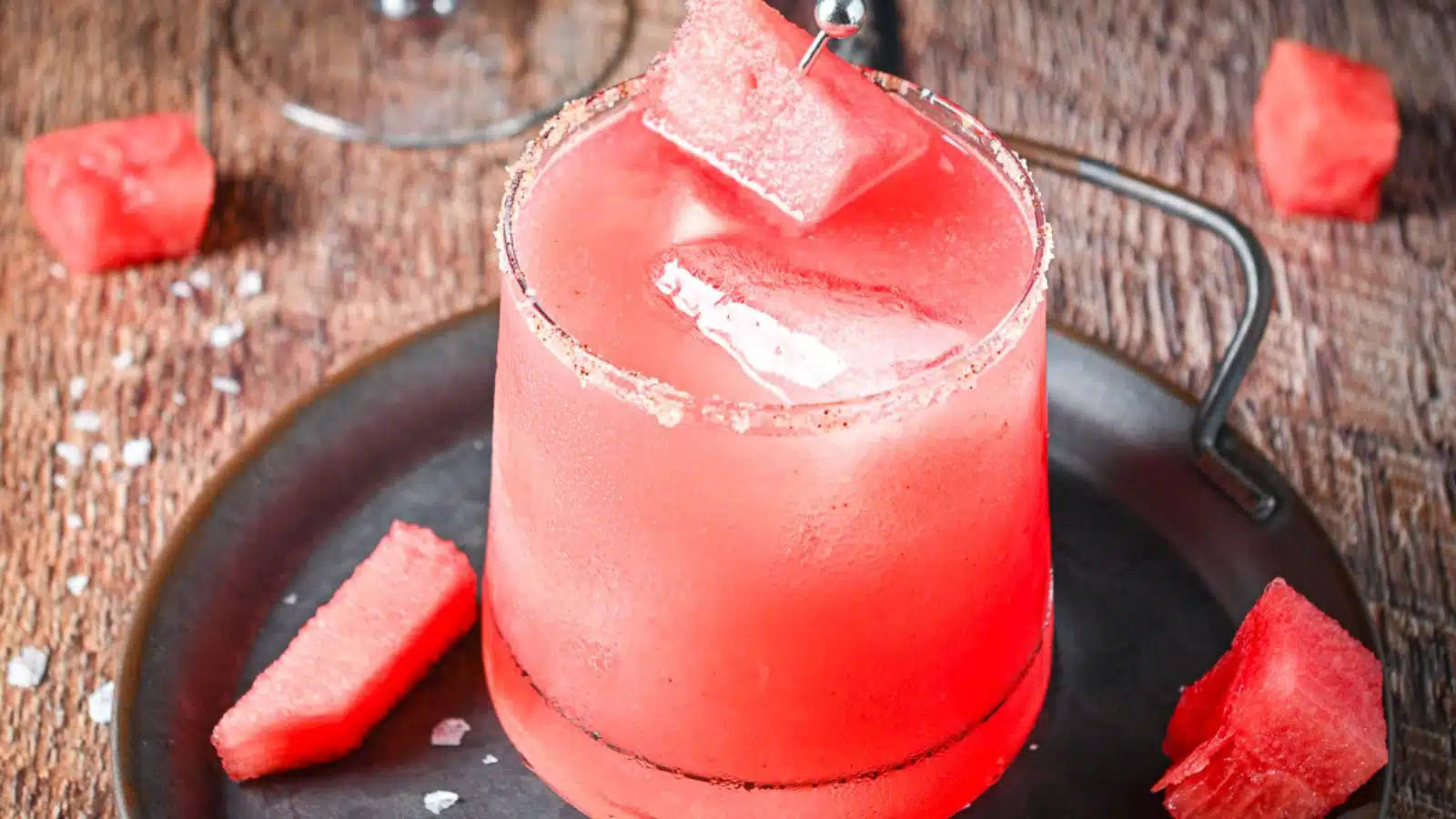A glass with salt on the rim and filled with a red margarita with watermelon as garnish