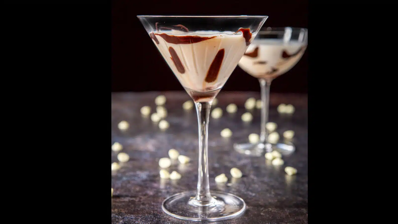 two martini glasses filled with white chocolate martini with dark chocolate dribbled down the glass