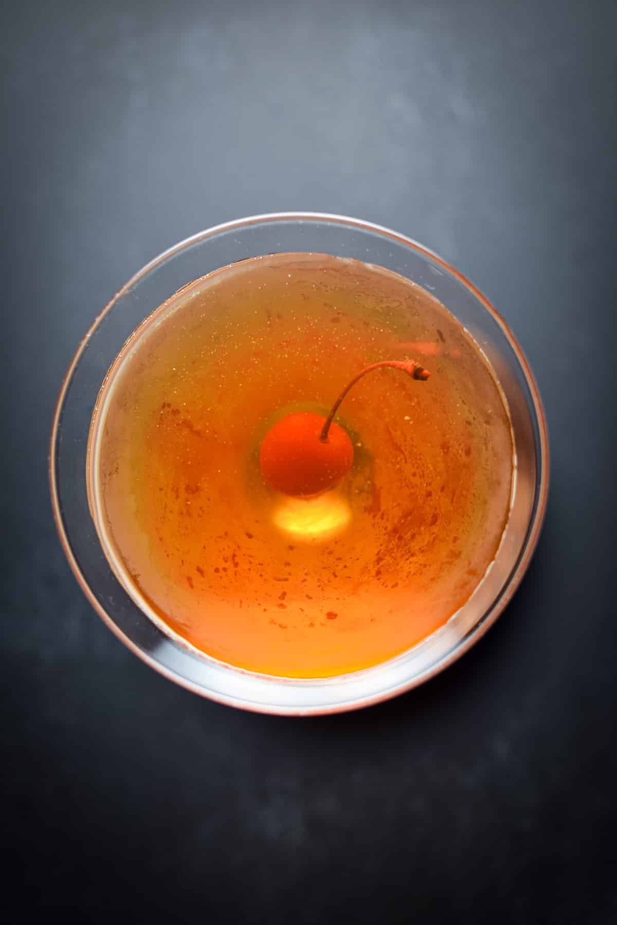 Overhead view of the reddish drink with a cherry in it