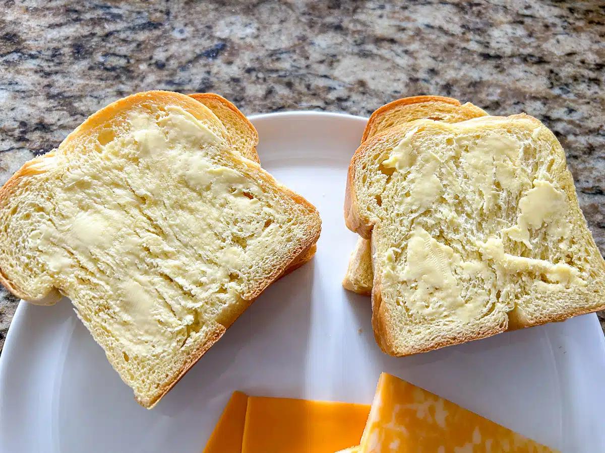 butter on two slices of bread with bread underneath and cheese at the bottom