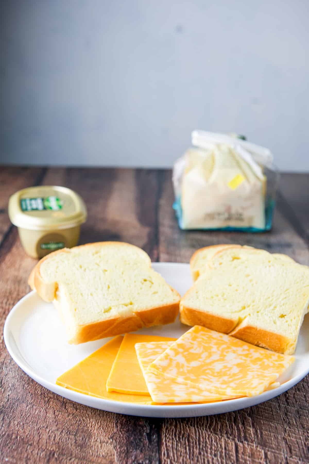 a white plate with sliced bread and cheese, with butter and the loaf of bread in the back