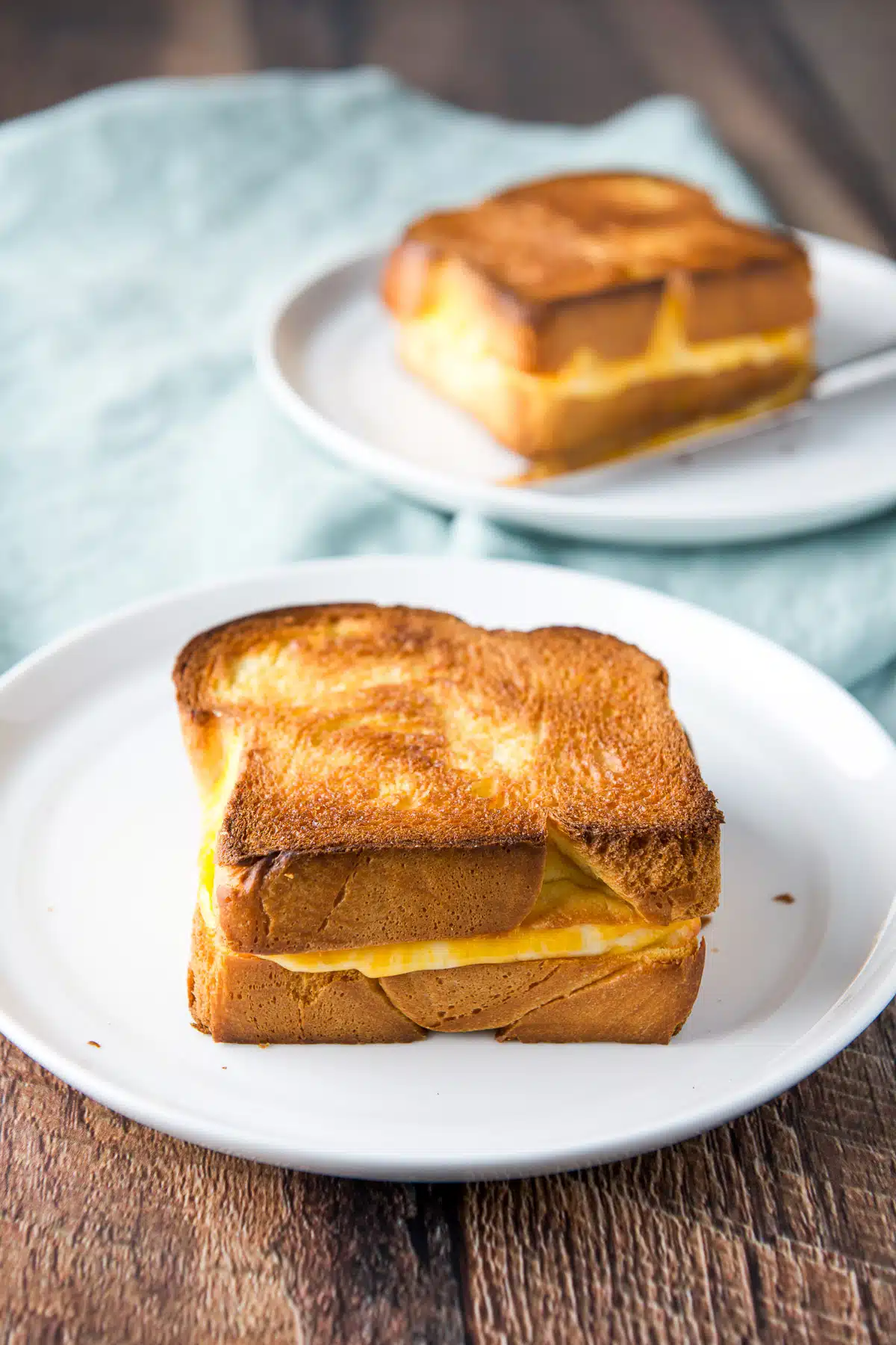 Two plates with grilled cheese on it on a table with a napkin
