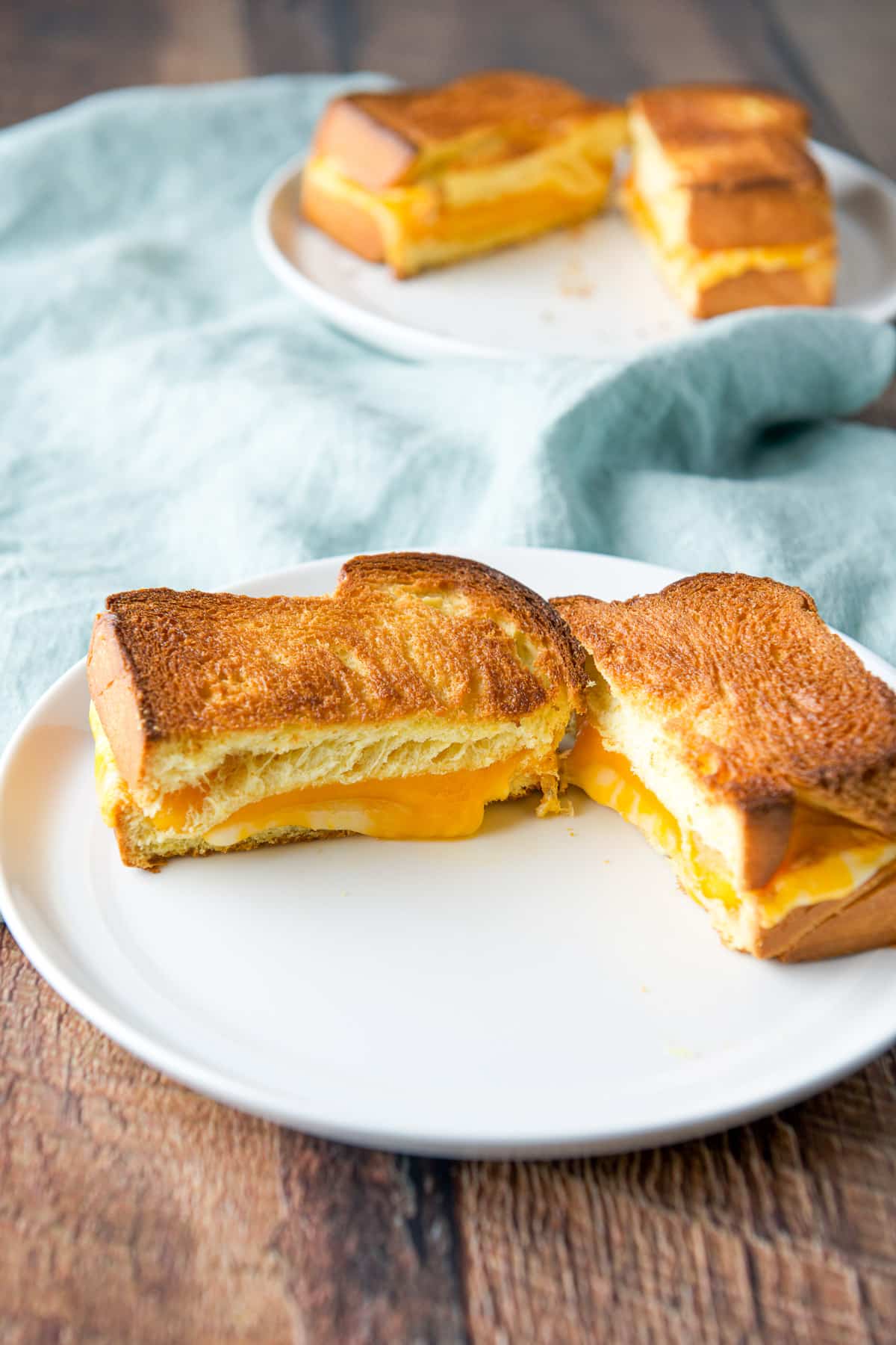 Two plates with cheese sandwiches cut in half on a green napkin
