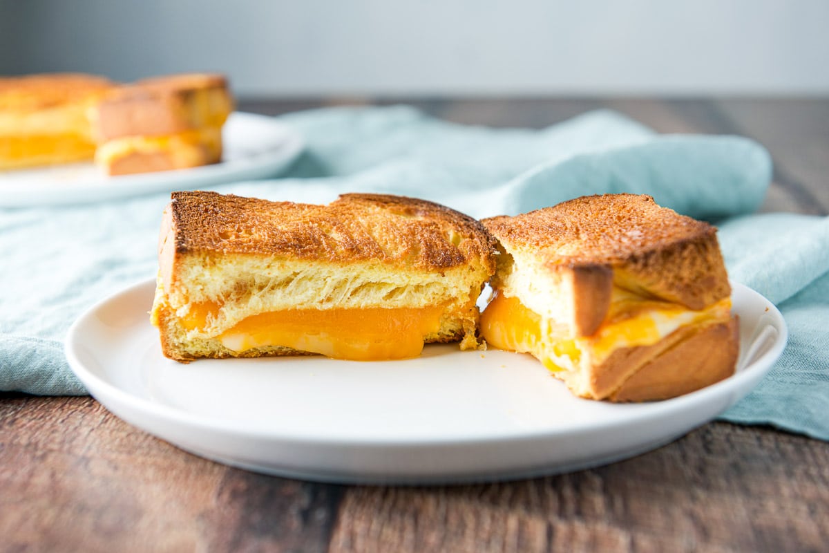 a horizontal photo of two white plates with a cheese sandwich cut in half