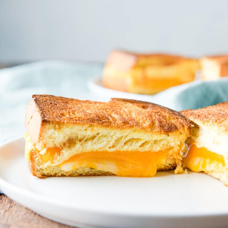 square photo of a white plate with a melted cheese in bread