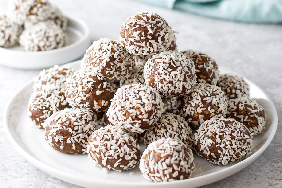 a white plate with a pyramid of booze balls covered in coconut on it wih a small plate in the back